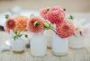 Small handmade white ceramic bud vases holding pink and coral dahlias on a woven table runner